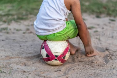 Çocuk oturuyor, kumda futbol oynuyor..