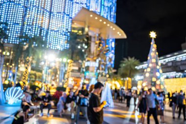 İnsanların mavi ve sarı tatil ışıklarının altında yürüdüğü bir gece sahnesi..