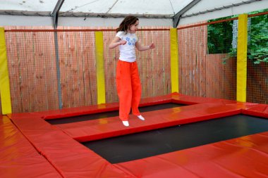 Mutlu kız trambolinde zıplarken eğleniyor. Sporcu kız trambolinde zıplıyor. Trambolinde zıplayan bir kızın açık hava çekimi, evde zıplamaktan hoşlanıyor. Mutlu yaz tatilleri. Yüksek kalite fotoğraf