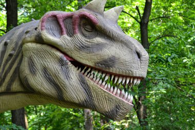 Jurasik dünyadan bir sahnede bir dinazor gösteriliyor. Parktaki dinozor modeli. Dev Tyrannosaurus parktaki bir sergide.