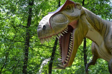 Jurasik dünyadan bir sahnede bir dinazor gösteriliyor. Parktaki dinozor modeli. Dev Tyrannosaurus parktaki bir sergide.