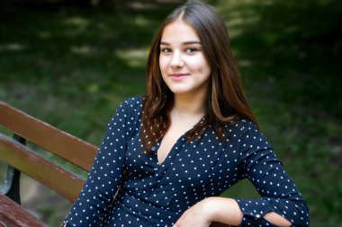 Emotional girl teenager with long hair hairstyle braids in a green shirt sits on a bench in the park. High quality photo