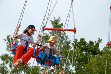 Çocuklar dönme dolapta zincirlerle, lunaparkta kayak broşürleriyle eğleniyorlar. Mutlu çocuklar, güneşli bir günde ikizler dışarıda eğleniyor. Yüksek kalite fotoğraf