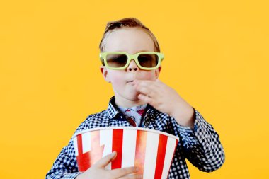 3-4 yaşlarında, kırmızı tişörtlü, elinde patlamış mısır kovası tutan, sarı arka planda izole edilmiş fast food yiyen sevimli bir çocuk. - Evet. Yüksek kalite fotoğraf