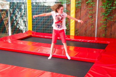 Mutlu kız trambolinde zıplarken eğleniyor. Sporcu kız trambolinde zıplıyor. Trambolinde zıplayan bir kızın açık hava çekimi, evde zıplamaktan hoşlanıyor. Mutlu yaz tatilleri.. 