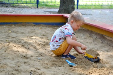 Dışarıda parkta kumların içinde oynayan tatlı bir çocuk. Güneşli sıcak yaz gününde güzel bir bebek eğleniyor. Yüksek kalite fotoğraf
