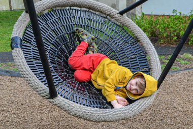 Küçük çocuk parkta salıncakta sallanırken eğleniyor. Mutlu çocuk sallanmaktan zevk alır. Şehirde çocuk için açık hava eğlencesi. Çocuk parkında salıncakta sallanan çocuğun yakın görüntüsü. 