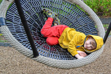 Küçük çocuk parkta salıncakta sallanırken eğleniyor. Mutlu çocuk sallanmaktan zevk alır. Şehirde çocuk için açık hava eğlencesi. Çocuk parkında salıncakta sallanan çocuğun yakın görüntüsü. 