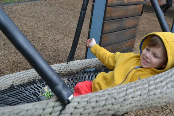 Küçük çocuk parkta salıncakta sallanırken eğleniyor. Mutlu çocuk sallanmaktan zevk alır. Şehirde çocuk için açık hava eğlencesi. Çocuk parkında salıncakta sallanan çocuğun yakın görüntüsü. 