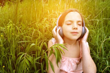 Çimlere uzanmış, parkta kulaklıkla müzik dinleyen rahat bir kadın. Parkta çimlerin üzerinde kulaklıkla müzik dinleyen küçük bir kız. Ön manzara. Yüksek kalite fotoğraf