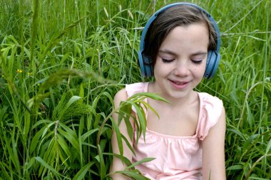 Çimlere uzanmış, parkta kulaklıkla müzik dinleyen rahat bir kadın. Parkta çimlerin üzerinde kulaklıkla müzik dinleyen küçük bir kız. Ön manzara. Yüksek kalite fotoğraf