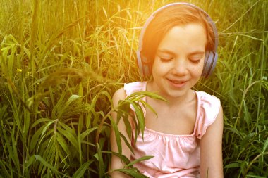 Çimlere uzanmış, parkta kulaklıkla müzik dinleyen rahat bir kadın. Parkta çimlerin üzerinde kulaklıkla müzik dinleyen küçük bir kız. Ön manzara. Yüksek kalite fotoğraf