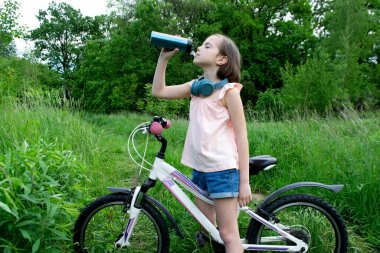 Genç kız bisikletçi yaz ormanı patikasında güneşin doğuşunun tadını çıkarıyor. Bisikletli kasklı mutlu küçük bir kızın yakın plan portresi. Yüksek kalite fotoğraf