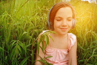 Çimlere uzanmış, parkta kulaklıkla müzik dinleyen rahat bir kadın. Parkta çimlerin üzerinde kulaklıkla müzik dinleyen küçük bir kız. Ön manzara. Yüksek kalite fotoğraf