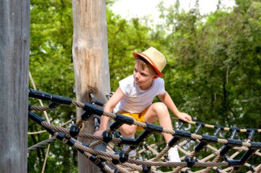 Bir çocuk, sıcak bir yaz gününde parktaki bir çocuk parkına tırmanır. Halk parkındaki çocuk parkı, çocuklar için eğlence ve eğlence, dağcılık eğitimi. Yüksek kalite fotoğraf