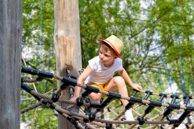 Bir çocuk, sıcak bir yaz gününde parktaki bir çocuk parkına tırmanır. Halk parkındaki çocuk parkı, çocuklar için eğlence ve eğlence, dağcılık eğitimi. Yüksek kalite fotoğraf