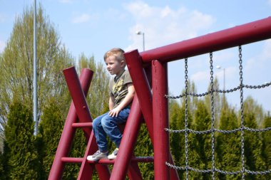 Bir çocuk, sıcak bir yaz gününde parktaki bir çocuk parkına tırmanır. Halk parkında çocuk parkı, çocuklar için eğlence ve eğlence, dağcılık eğitimi. 