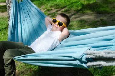 Sarışın, sevimli beyaz çocuk bahçedeki ya da bahçedeki renkli hamakta rahatlıyor ve eğleniyor. Çocuklar için yaz tatili. Hamakta sallanan çocuk. Çocuklar için etkinlikler. Yüksek kalite fotoğraf