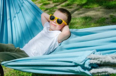 Sarışın, sevimli beyaz çocuk bahçedeki ya da bahçedeki renkli hamakta rahatlıyor ve eğleniyor. Çocuklar için yaz tatili. Hamakta sallanan çocuk. Çocuklar için etkinlikler. Yüksek kalite fotoğraf
