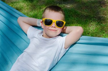 Sarışın, sevimli beyaz çocuk bahçedeki ya da bahçedeki renkli hamakta rahatlıyor ve eğleniyor. Çocuklar için yaz tatili. Hamakta sallanan çocuk. Çocuklar için etkinlikler. Yüksek kalite fotoğraf