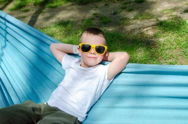 Sarışın, sevimli beyaz çocuk bahçedeki ya da bahçedeki renkli hamakta rahatlıyor ve eğleniyor. Çocuklar için yaz tatili. Hamakta sallanan çocuk. Çocuklar için etkinlikler. Yüksek kalite fotoğraf