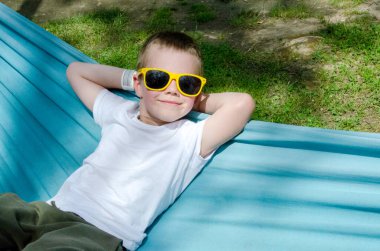 Sarışın, sevimli beyaz çocuk bahçedeki ya da bahçedeki renkli hamakta rahatlıyor ve eğleniyor. Çocuklar için yaz tatili. Hamakta sallanan çocuk. Çocuklar için etkinlikler. Yüksek kalite fotoğraf