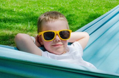 Sarışın, sevimli beyaz çocuk bahçedeki ya da bahçedeki renkli hamakta rahatlıyor ve eğleniyor. Çocuklar için yaz tatili. Hamakta sallanan çocuk. Çocuklar için etkinlikler. Yüksek kalite fotoğraf