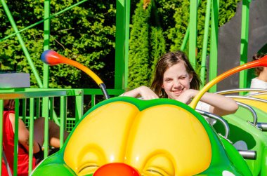 Mutlu kız atlı karıncaya biniyor. Lunaparkta eğlenirken gülerek, gülümseyerek, neşeyle el sallayarak hız trenine binme hızıyla. Yüksek kalite fotoğraf