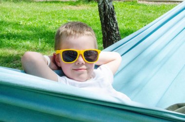 Sarışın, sevimli beyaz çocuk bahçedeki ya da bahçedeki renkli hamakta rahatlıyor ve eğleniyor. Çocuklar için yaz tatili. Hamakta sallanan çocuk. Çocuklar için etkinlikler. Yüksek kalite fotoğraf