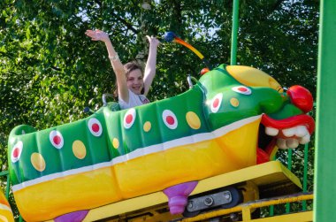 Mutlu kız atlı karıncaya biniyor. Lunaparkta eğlenirken gülerek, gülümseyerek, neşeyle el sallayarak hız trenine binme hızıyla. Yüksek kalite fotoğraf