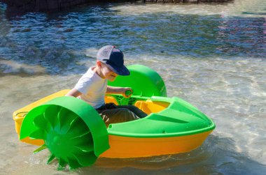 Çocuk su kayığı oynuyor. Yumuşak odaklanma. Küçük bir kız, tatil köyündeki bir havuzda renkli bir tekneye biniyor. Yüksek kalite fotoğraf. 