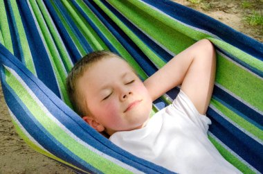 Sarışın, sevimli beyaz çocuk bahçedeki ya da bahçedeki renkli hamakta rahatlıyor ve eğleniyor. Çocuklar için yaz tatili. Hamakta sallanan çocuk. Çocuklar için etkinlikler. Yüksek kalite fotoğraf