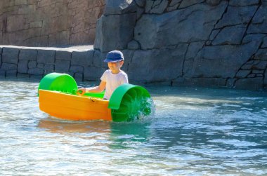 Çocuk su kayığı oynuyor. Yumuşak odaklanma. Küçük bir kız, tatil köyündeki bir havuzda renkli bir tekneye biniyor. Yüksek kalite fotoğraf. 