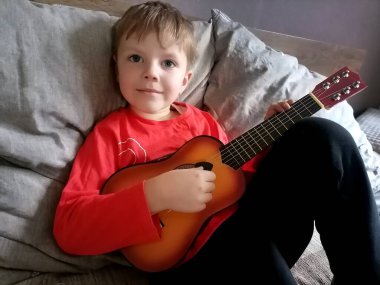 Kırmızı ekose gömlekli, ciddi ve keyifli bir çocuk kırmızı elektro gitar çalmayı öğrenir. Çocuk müzik öğreniyor. Yüksek kalite fotoğraf