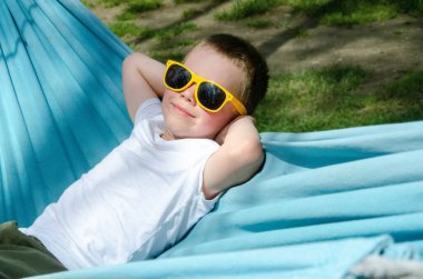 Sarışın, sevimli beyaz çocuk bahçedeki ya da bahçedeki renkli hamakta rahatlıyor ve eğleniyor. Çocuklar için yaz tatili. Hamakta sallanan çocuk. Çocuklar için etkinlikler. Yüksek kalite fotoğraf
