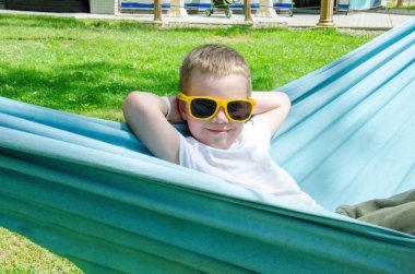 Sarışın, sevimli beyaz çocuk bahçedeki ya da bahçedeki renkli hamakta rahatlıyor ve eğleniyor. Çocuklar için yaz tatili. Hamakta sallanan çocuk. Çocuklar için etkinlikler. Yüksek kalite fotoğraf