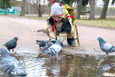 Yeşil lastik çizmeli şirin çocuk banktan güvercinleri besliyor. Tonlama ve seçici odaklanma ile görüntü. Bir çocuk parkta güvercinleri besler. Yüksek kalite fotoğraf