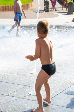 Park çeşmesinde suyla oynayan bir çocuk. Sıcak yaz. Küçük çocuk, güneşli yaz gününde kuru çeşmedeki su jetlerinin arasında oynuyor. Şehirdeki çocuklar için aktif yaz tatili. Yüksek kalite fotoğraf