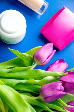 Anneler Günü için şık bir hediye. Yüksek topuklu ayakkabılar, el çantası, hediye kutusu, lale çiçekleri, ruj, makyaj fırçası ve kartpostallı açık zarf eşliğinde pastel bej arka planda bulunan küpeler. Yüksek kalite fotoğraf