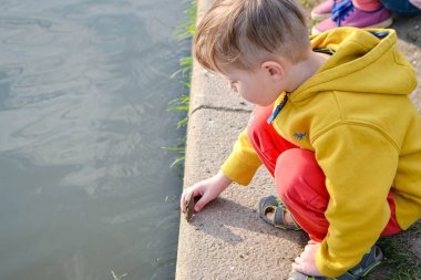 Küçük çocuk arka bahçedeki gölete balık besliyor. Küçük bir çocuk yazın kağıt botu suya indiriyor. Yüksek kalite fotoğraf