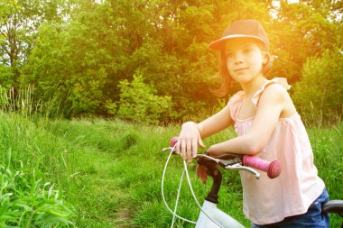 Genç kız bisikletçi yaz ormanı patikasında güneşin doğuşunun tadını çıkarıyor. Bisikletli kasklı mutlu küçük bir kızın yakın plan portresi. Yüksek kalite fotoğraf