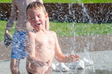 Park çeşmesinde suyla oynayan bir çocuk. Sıcak yaz. Küçük çocuk, güneşli yaz gününde kuru çeşmedeki su jetlerinin arasında oynuyor. Şehirdeki çocuklar için aktif yaz tatili. Yüksek kalite fotoğraf