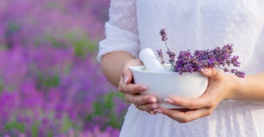 A bottle of lavender essential oil on a wooden table and a field of flowers background. selective focus