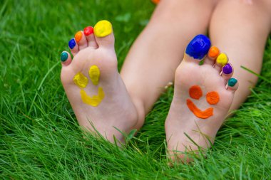 Yeşil çimlerin üzerinde gülümseyen boya desenli çocuk ayakları. Seçici odaklanma. Doğa.