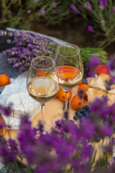 stock image Wicker basket with delicious food for a romantic picnic in a lavender field. The girl pours wine. Selective focus