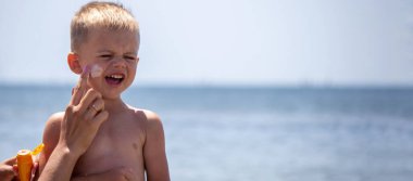 Çocuğun yüzünde ve sırtında güneş kremi var. Denizin arka planında. Seçici odak