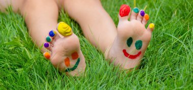 Yeşil çimlerin üzerinde gülümseyen boya desenli çocuk ayakları. Seçici odaklanma. Doğa.