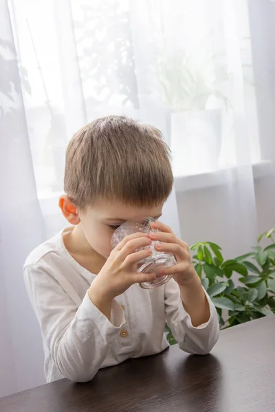 stock image Cute little boy drinks water from a glass. Selective focus