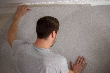 Bir adam duvar kağıtlarını yapıştırıyor, evi onarıyor. Seçici odak
