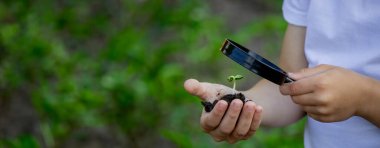 Çocuk elinde filizle toprağı tutuyor ve büyüteçle bakıyor. Seçici odak